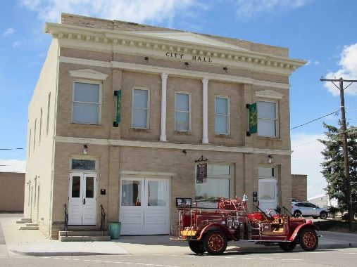 A two-story municipal building with an old vehicle out front