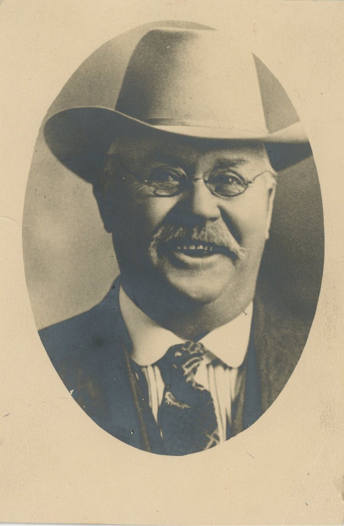 Black and white photograph of a man wearing a hat and glasses.