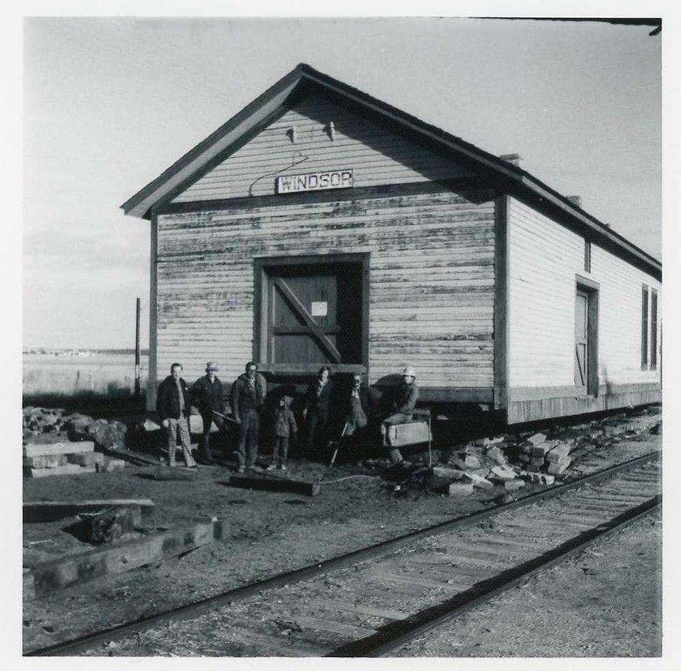 Black and white photograph of a group of men standing in front of a train depot.