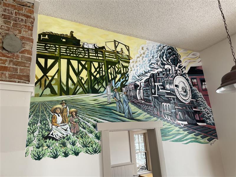 Color photograph of a mural depicting a train and people working in sugar beet fields.